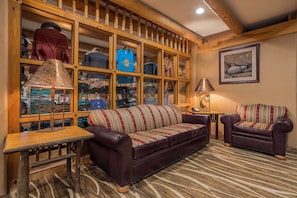 A cozy living room with a leather sofa, a patterned armchair, and a wooden display cabinet filled with various items.