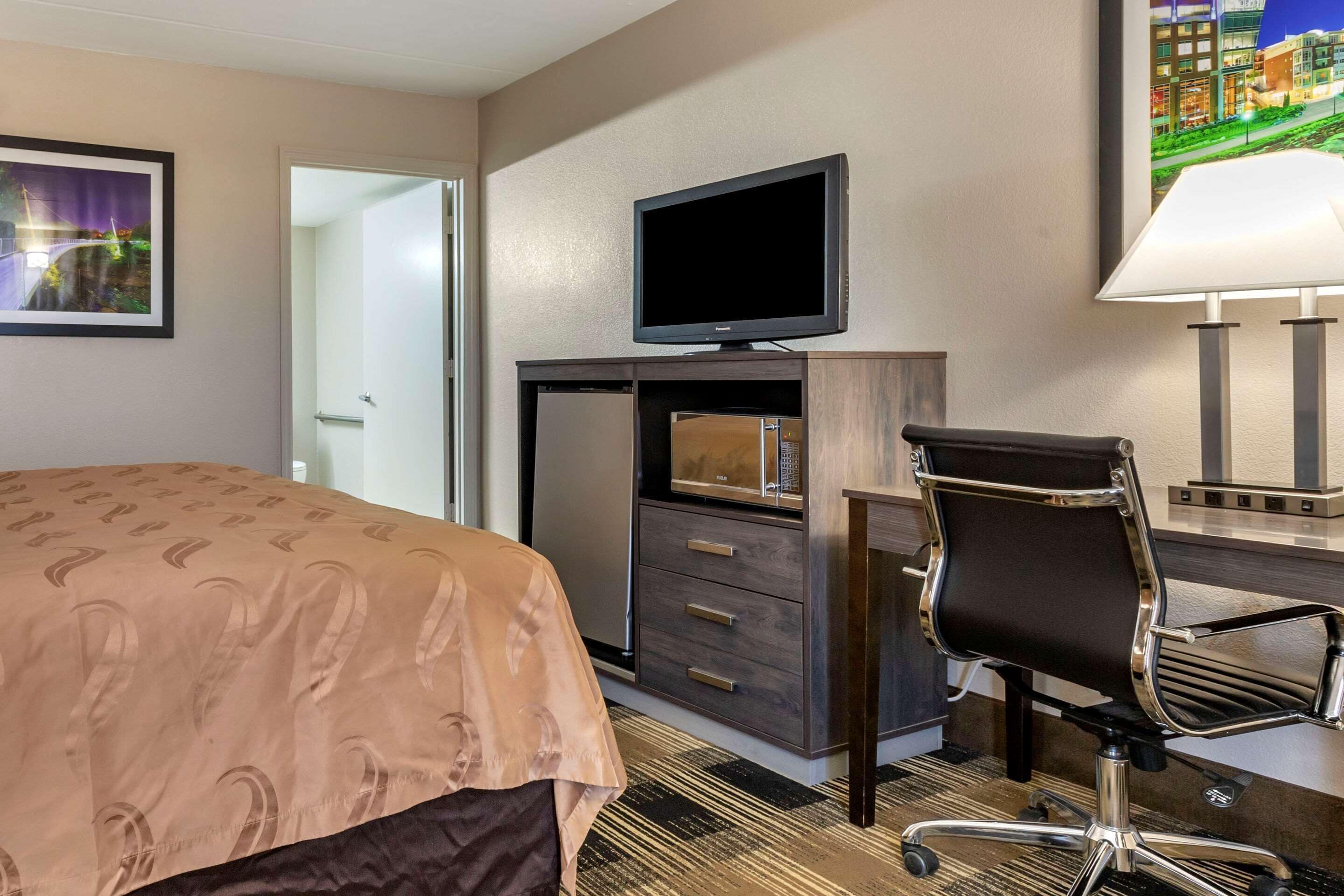 Une chambre d’hôtel comprenant un lit, un bureau avec un ordinateur, une télévision et une lampe.