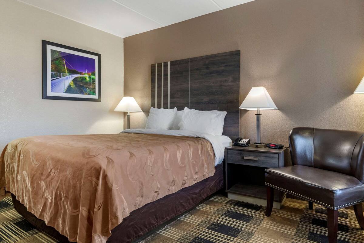 Habitación de hotel con una cama grande, dos lámparas de noche, una silla, una mesita de noche y un cuadro en la pared.