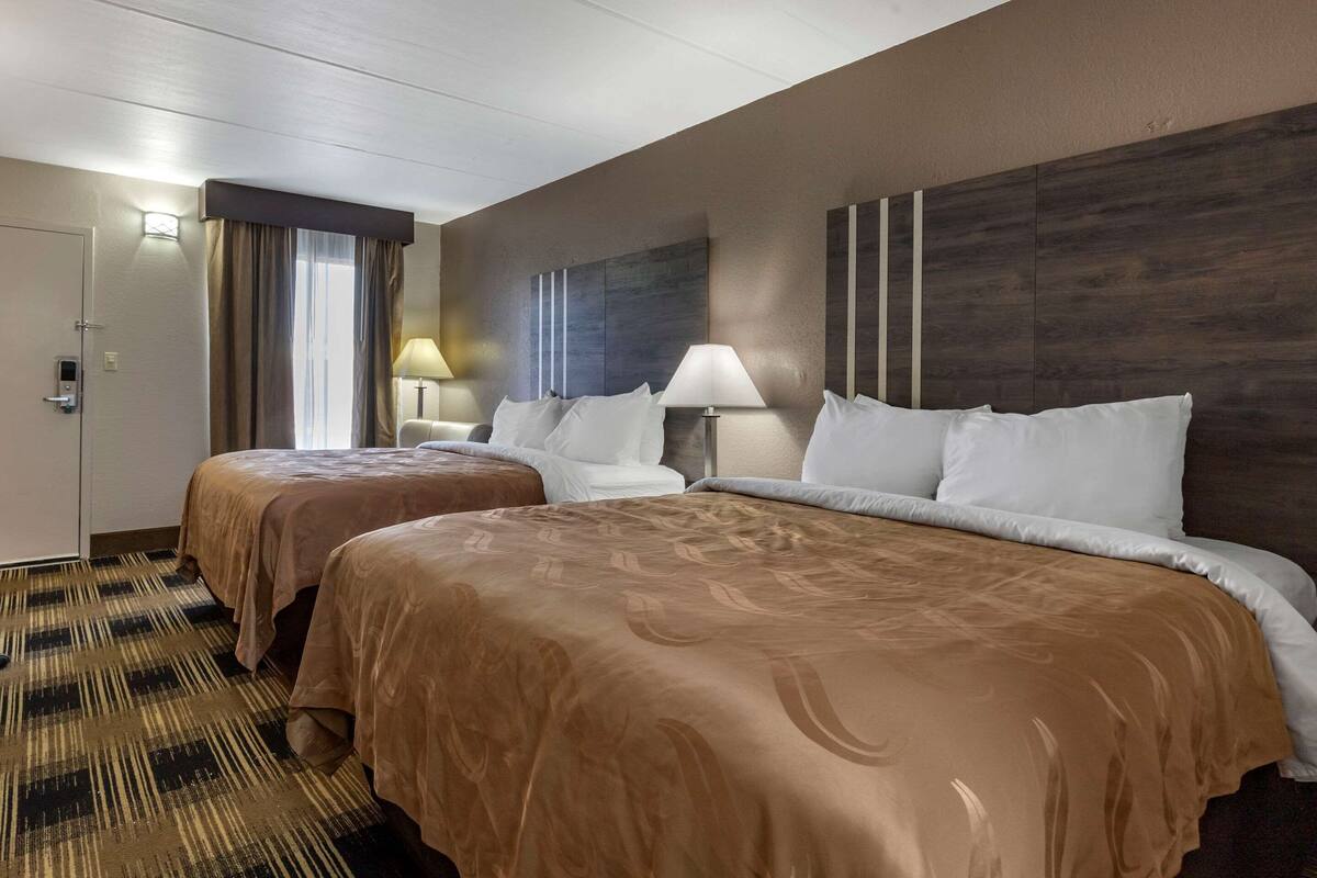 Una habitación de hotel con dos camas, un ventanal con cortinas, una obra de arte en la pared y piso alfombrado.