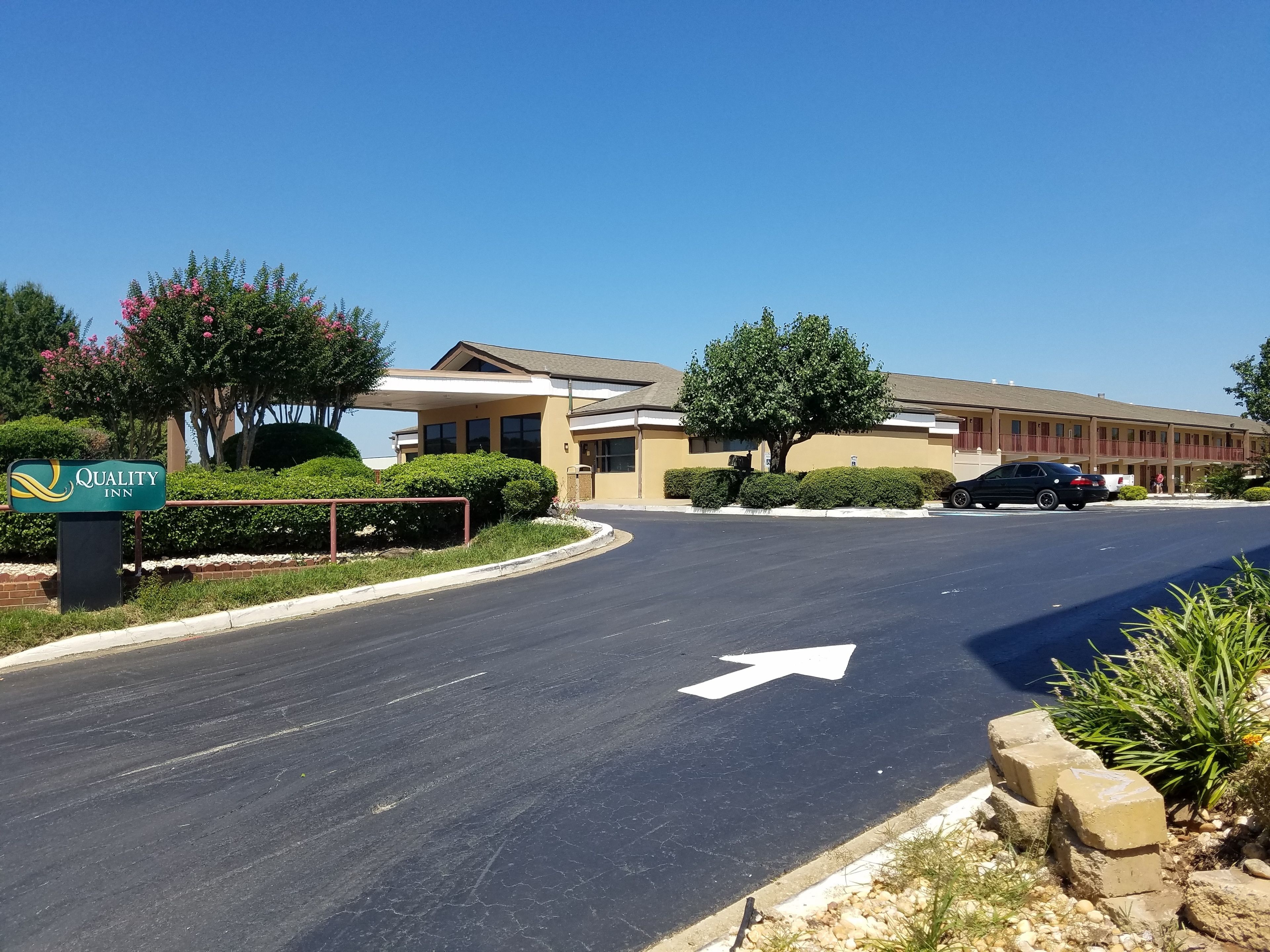 A Quality Inn hotel with a clear road, directional arrow, and well-maintained landscaping.