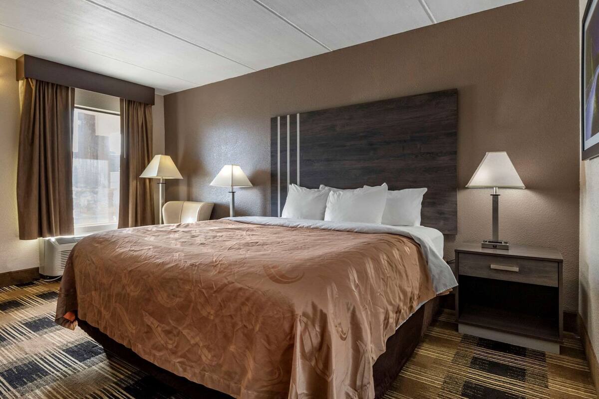 Una habitación de hotel con una cama grande, dos lámparas de noche, una silla y una mesita de noche.