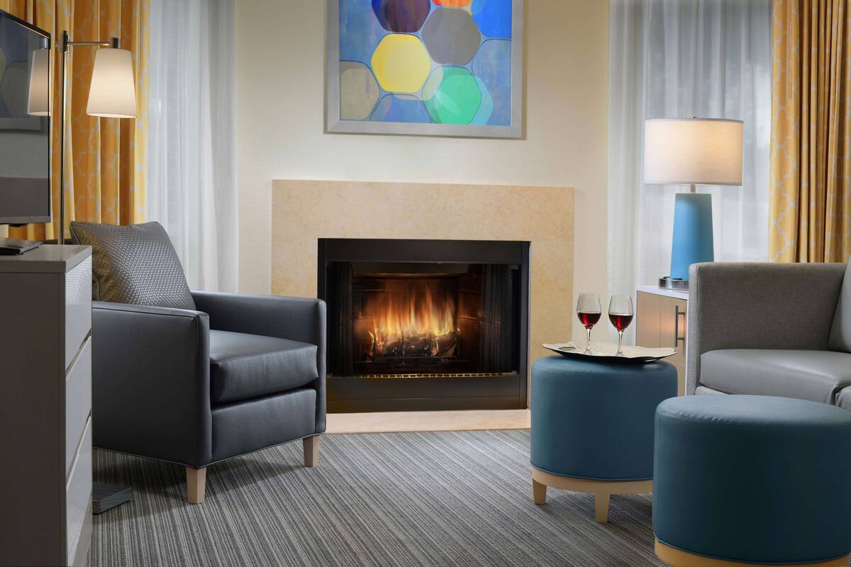 Una sala de estar moderna con chimenea, dos sillones, otomanas y una mesita de centro con copas de vino.