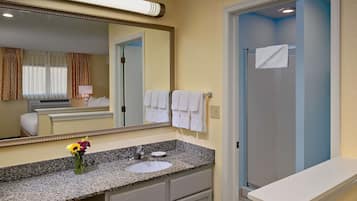 Un baño de hotel con encimera de granito, lavabo, espejo y zona de ducha.