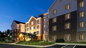 Ein mehrstöckiges Hotel mit roten Backsteinelementen und Stuckfassade, ausgestattet mit einem zentralen Eingangsbereich und einer überdachten Veranda, vor dem sich ein Parkplatz befindet.
