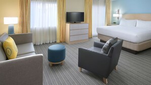 Ein Hotelzimmer mit einem Bett, zwei Sesseln, einer Couch, einem Fernseher auf einem Schrank und einer Lampe.