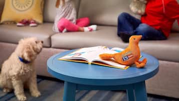 Un salón con un sofá, una mesita redonda con un libro y un peluche, y un perro.