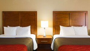A hotel room with two beds, a nightstand with a lamp, and a wooden headboard.