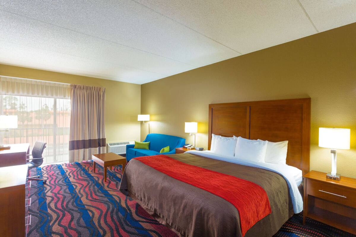 A hotel room with a large bed, a desk, a chair, and a window with curtains.