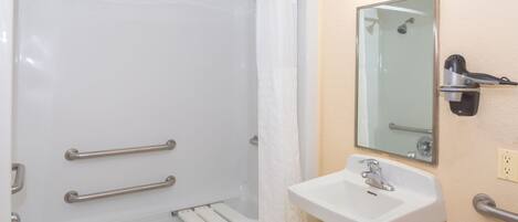 Une salle de bain équipée d’une douche, de barres d’appui, d’un lavabo et d’un miroir.