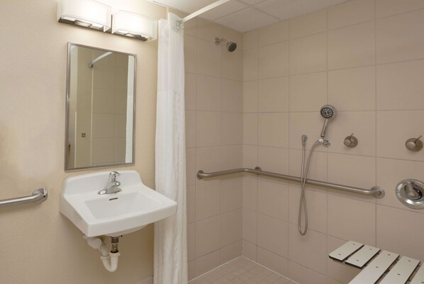 A bathroom with a sink, mirror, shower, and grab bars.