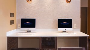 Two Apple iMac computers on a white desk with a textured wall behind them.