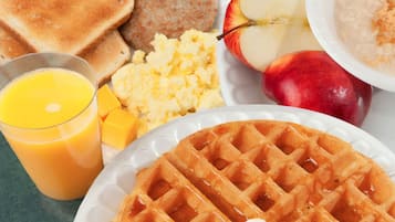 Une assiette de petit-déjeuner comprenant des toasts, des œufs brouillés, des saucisses, des tranches de pomme et une gaufre.