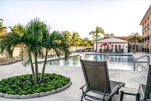 A pool area with lounge chairs, palm trees, and a building in the background.
