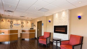 A reception area with a wooden reception desk, two red chairs, a small table, and a stone wall with a mounted screen.