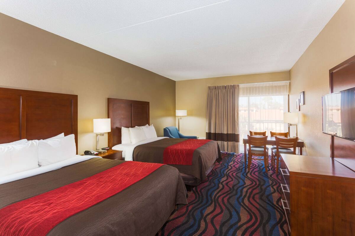 A hotel room with two beds, a desk, a chair, a TV, and a window with curtains.