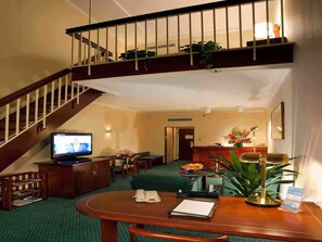 A hotel lobby with a staircase, a television, a reception desk, a seating area, and a reception desk with a plant.