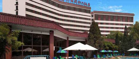 A hotel with a swimming pool, multiple lounge chairs, and umbrellas.
