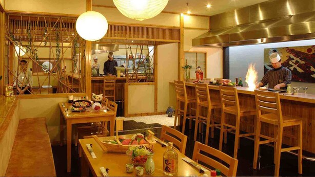 Un restaurante con interiores de madera, una barra de sushi y un chef preparando comida.