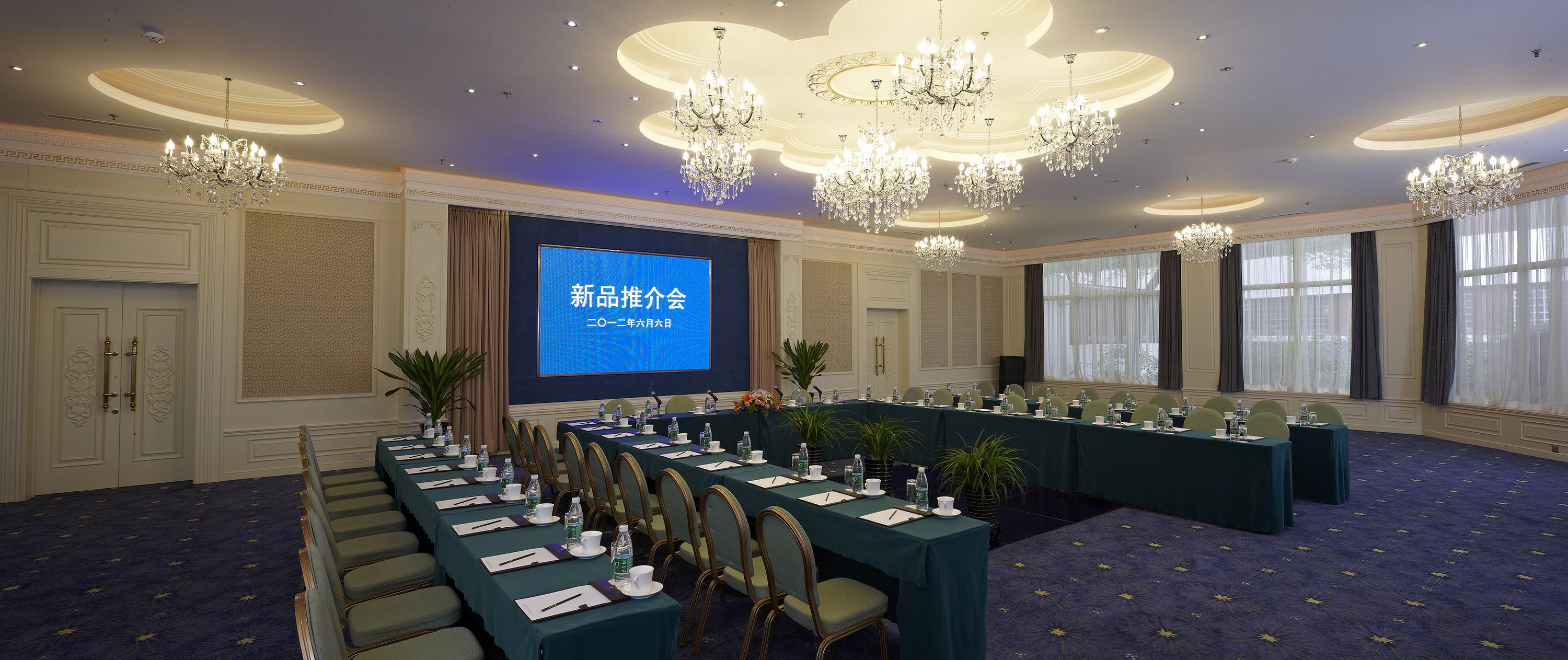 Un salón de conferencias con una pantalla grande mostrando texto, varias mesas con sillas y candelabros.