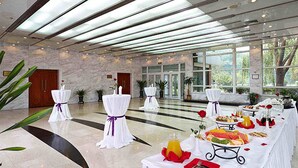 Un espacio interior amplio con una larga mesa dispuesta para una comida, ventanas grandes y una pared de piedra.