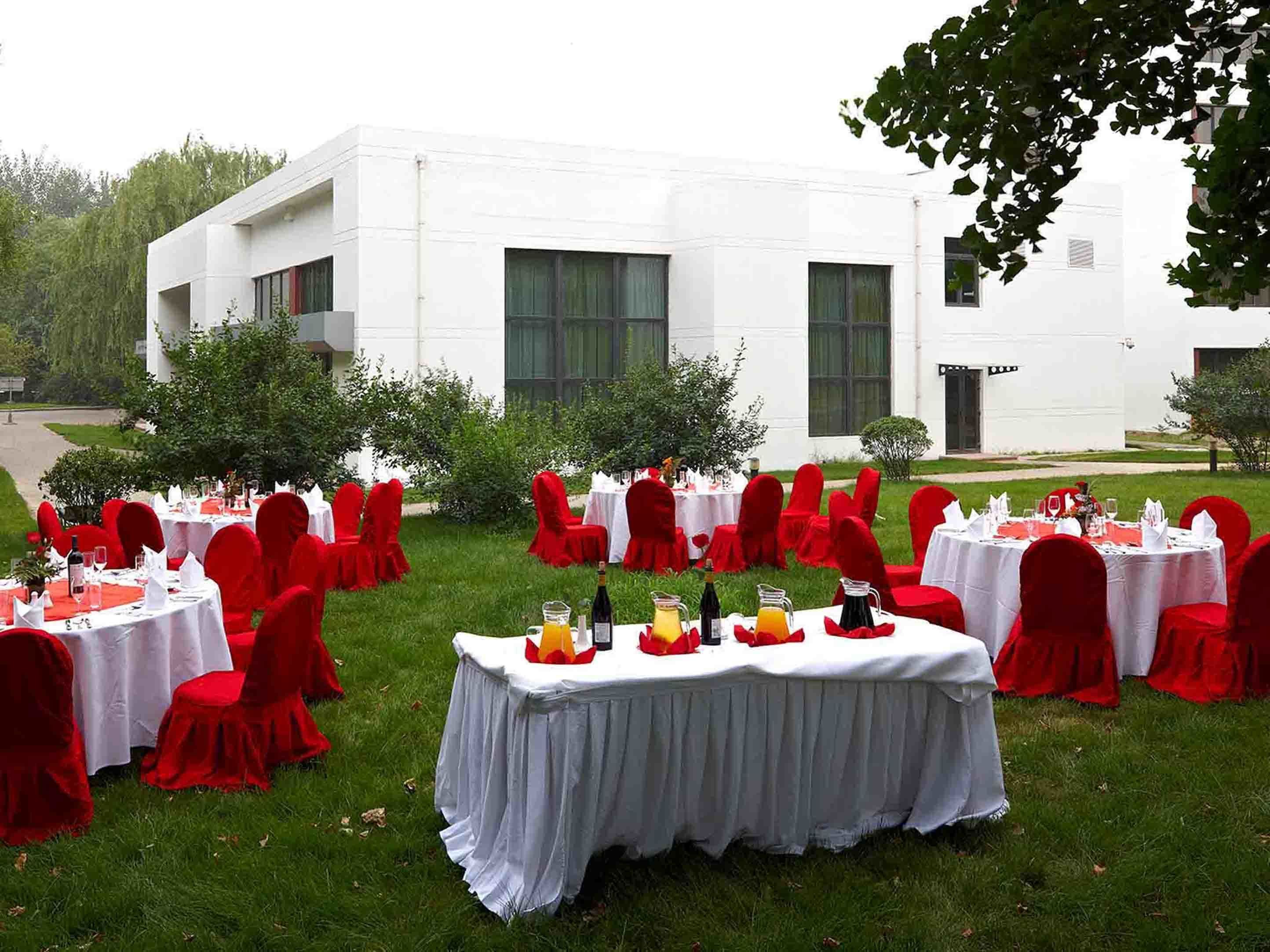 Un espace extérieur aménagé pour les événements, avec plusieurs tables rondes recouvertes de nappes blanches, entourées de chaises rouges.