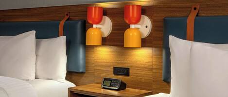 A hotel room with two beds, a wooden headboard, a nightstand with a clock, and wall-mounted lamps.