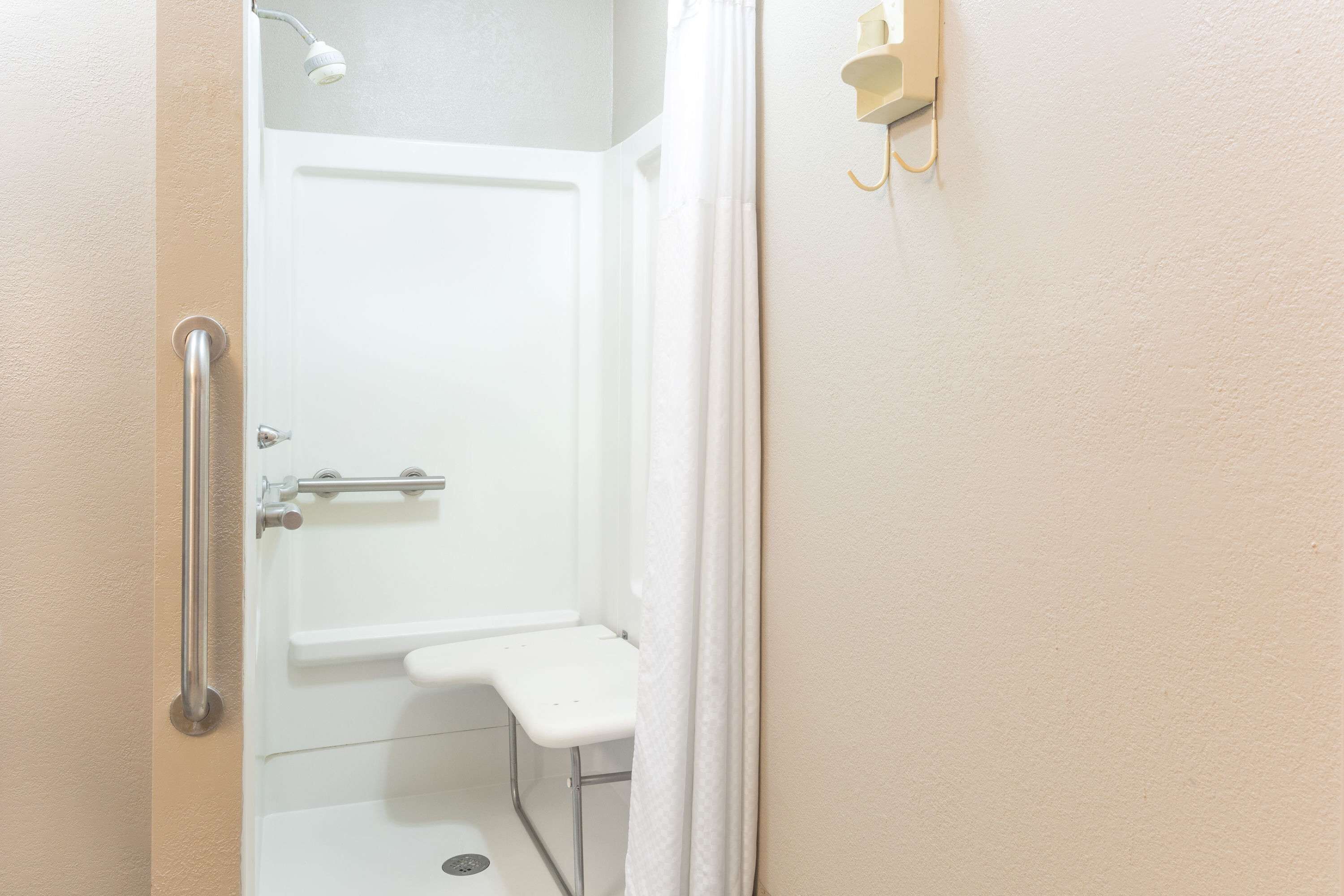 A small, white bathroom with a shower, a toilet, and a handrail.
