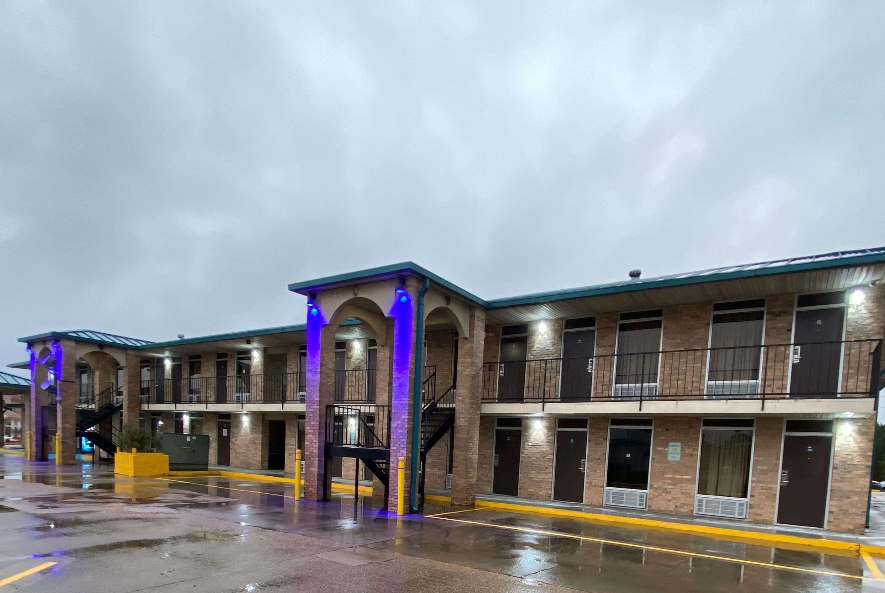 Un motel de varios pisos con fachada de ladrillo, múltiples balcones y suelo mojado que indica lluvia reciente.