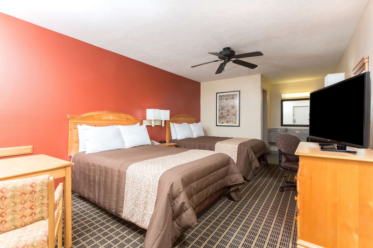 Quarto de hotel com duas camas, uma escrivaninha, televisão e ventoinha no teto.