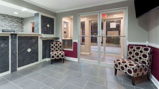 A reception area with a marble counter, two patterned chairs, and a glass door leading outside. - Days Inn by Wyndham Forest (Forest)