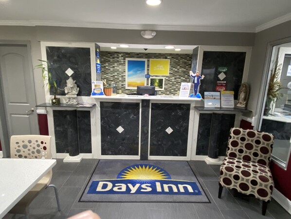 A reception area with a marble counter, a 'Days Inn' logo on the floor mat, and a statue of a deity on the left.