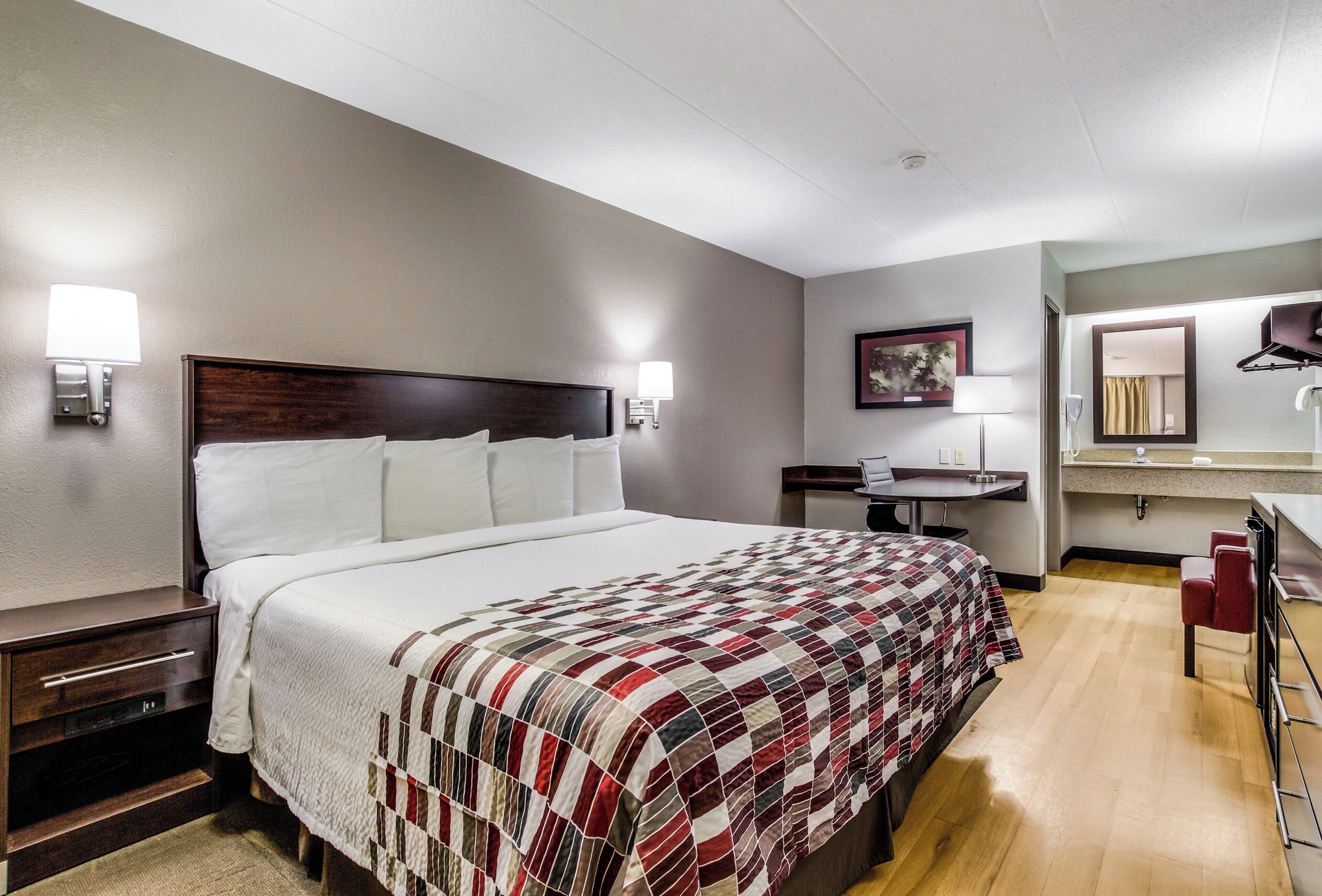 A hotel room with a large bed, bedside tables, a desk, a chair, a mirror, and a bathroom.