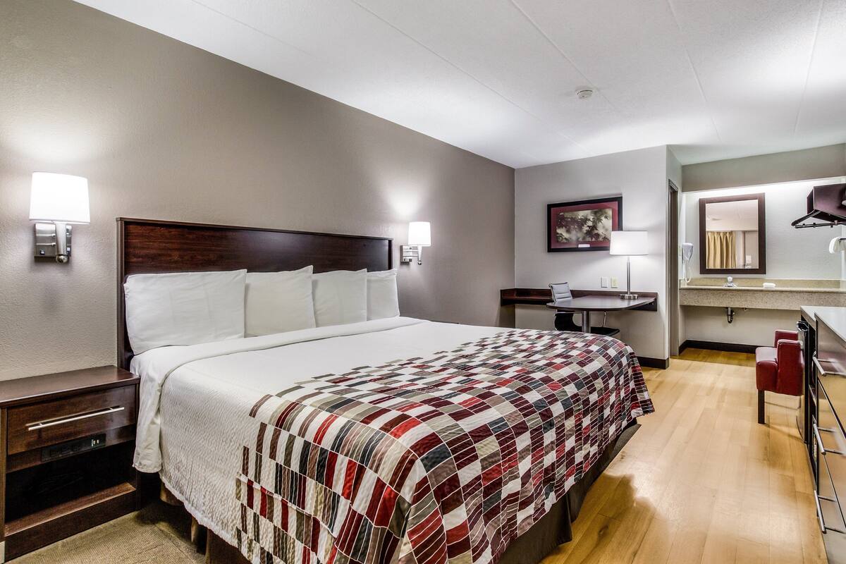 Ein Hotelzimmer mit einem großen Bett, Nachttischen, einem Schreibtisch, einem Sessel und einem Badezimmer.