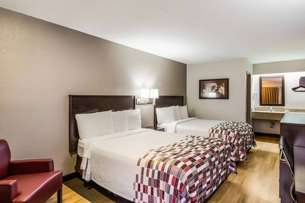Ein Hotelzimmer mit zwei Betten, einem Schreibtisch, einem Stuhl, einem Spiegel und einem Bild an der Wand.