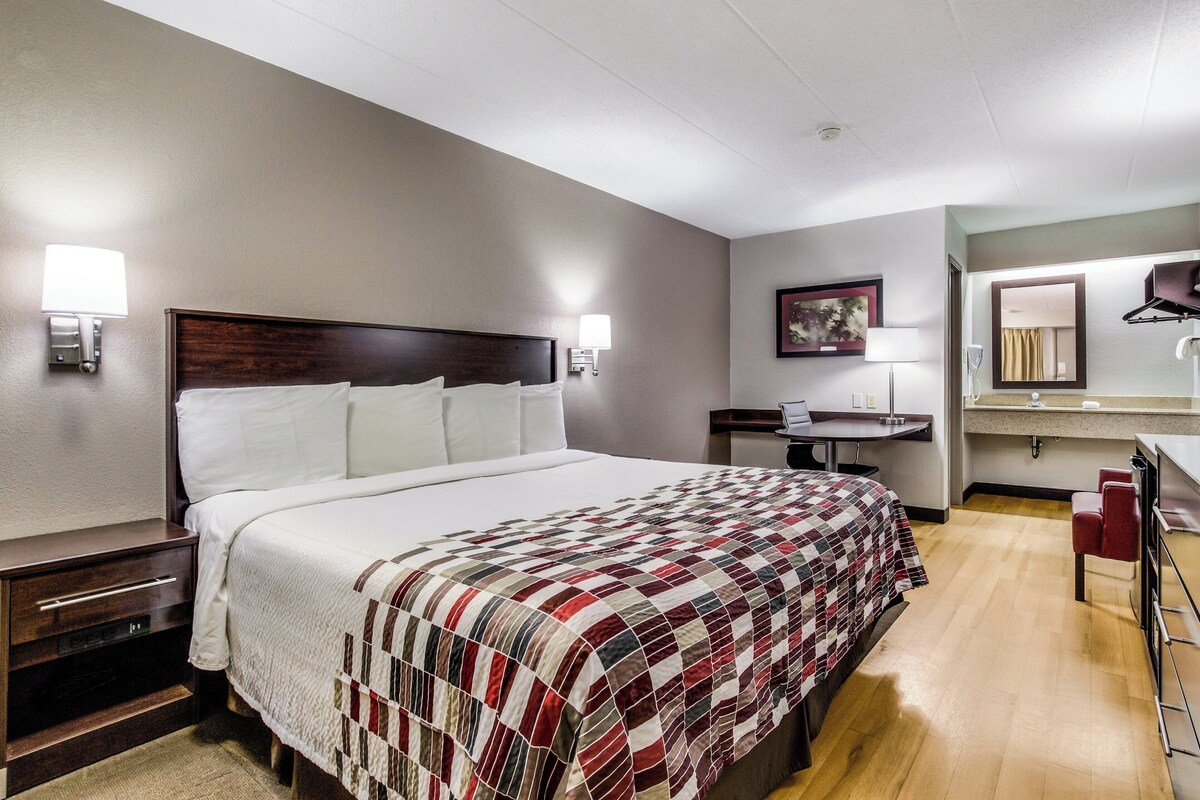 A hotel room with a large bed, bedside tables, a desk, a mirror, and a bathroom.