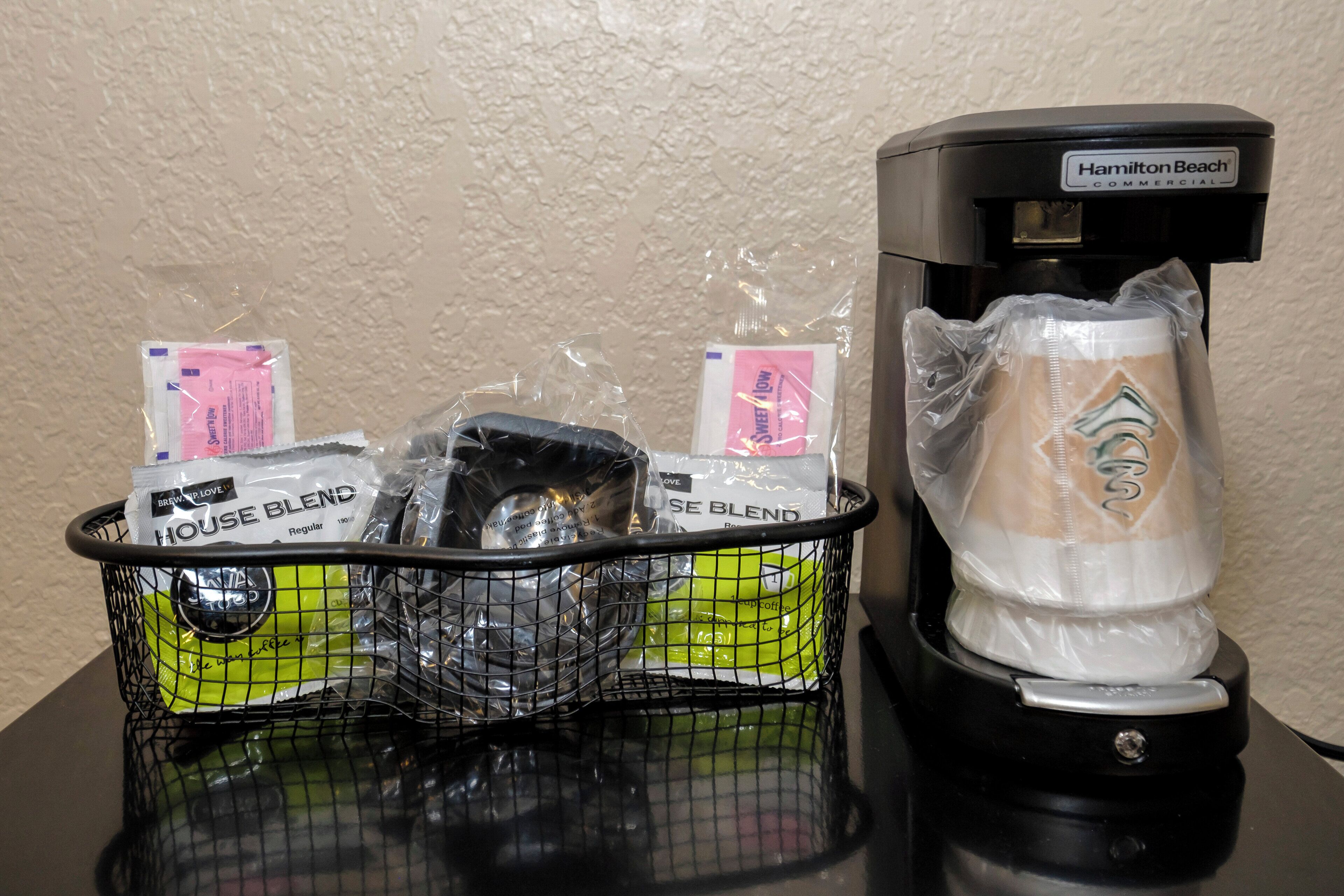 A coffee maker and a basket with coffee pods and a reusable cup on a table.
