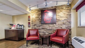 A Red Roof Inn lobby with a stone wall, two leather chairs, a coffee station, and a sign. - Red Roof Inn Lexington (Lexington)