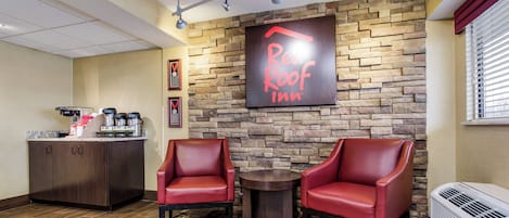 A Red Roof Inn lobby with a stone wall, two leather chairs, a coffee station, and a sign.