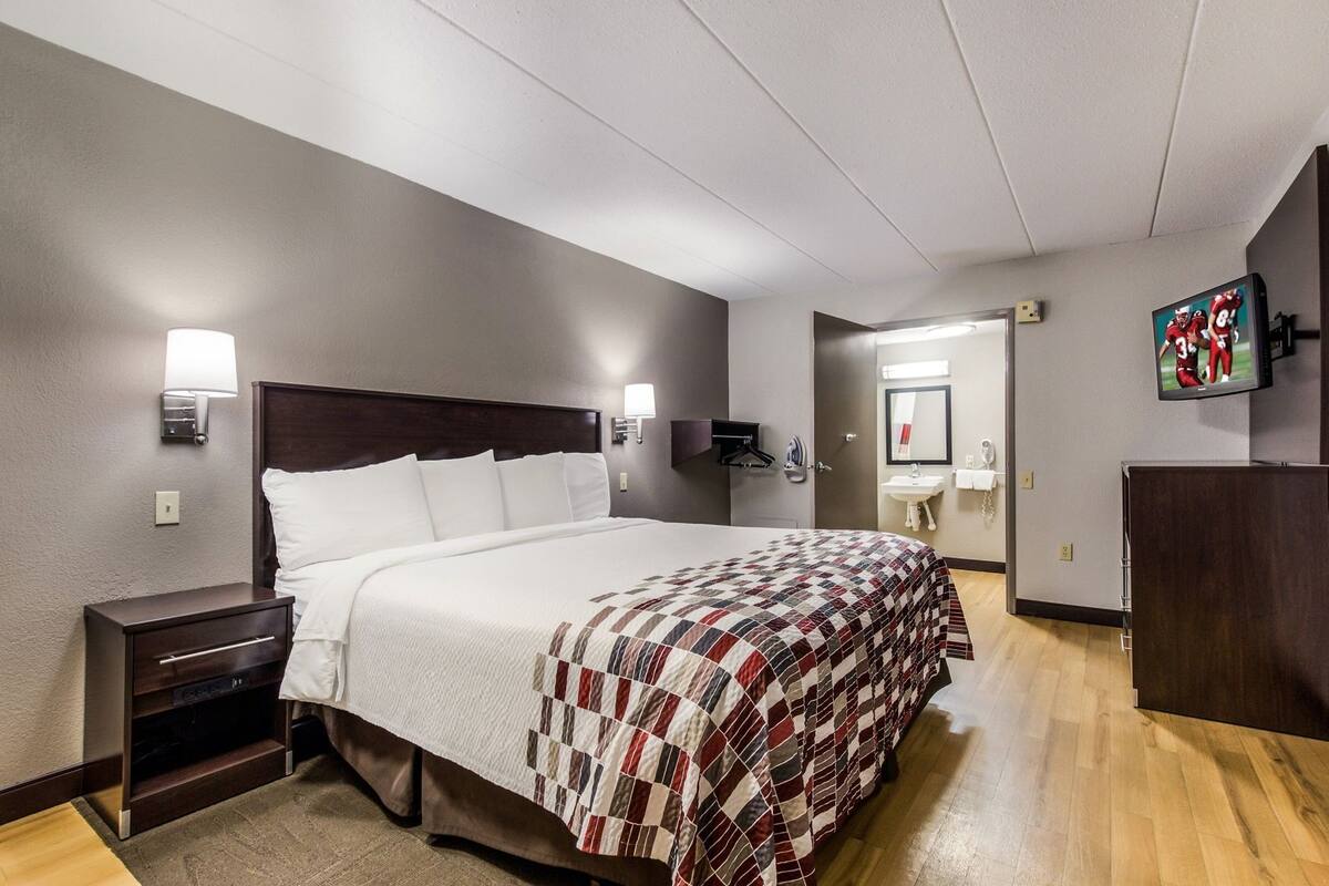 Ein Hotelzimmer mit einem großen Bett, Nachttischen, einem Spiegel, einem Fernseher und einem Kleiderschrank.