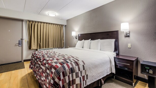 A hotel room with a bed, bedside tables, a wall-mounted lamp, and a door with a curtain. - Red Roof Inn Lexington (Lexington)