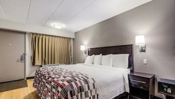 Habitación de hotel con cama, mesitas de noche, lámpara de pared y una puerta con cortina.