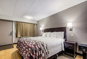 Habitación de hotel con cama, mesitas de noche, lámpara de pared y una puerta con cortina.