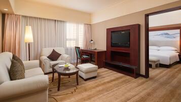 A hotel room with a sofa, armchair, a small table with a lamp, a TV, and a bed.
