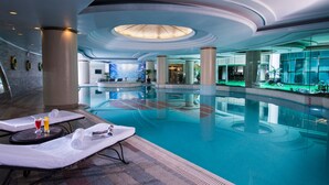A spacious indoor swimming pool with lounge chairs, a central column, and a modern ceiling design. - Sunshine Hotel Shenzhen (Shenzhen)