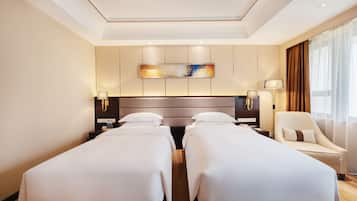 A hotel room with two single beds, a large painting on the wall, a sofa, and a large window with curtains.