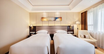 A hotel room with two single beds, a large painting on the wall, a sofa, and a large window with curtains.