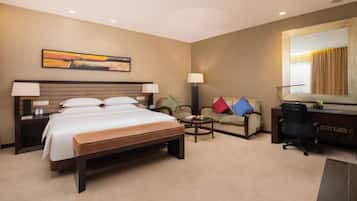 Habitación de hotel con una cama grande, un escritorio, una silla, una mesita y un sofá.