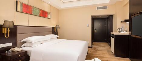 A hotel room with a large bed, bedside lamps, a desk with a telephone, a bowl of fruit, and a TV.