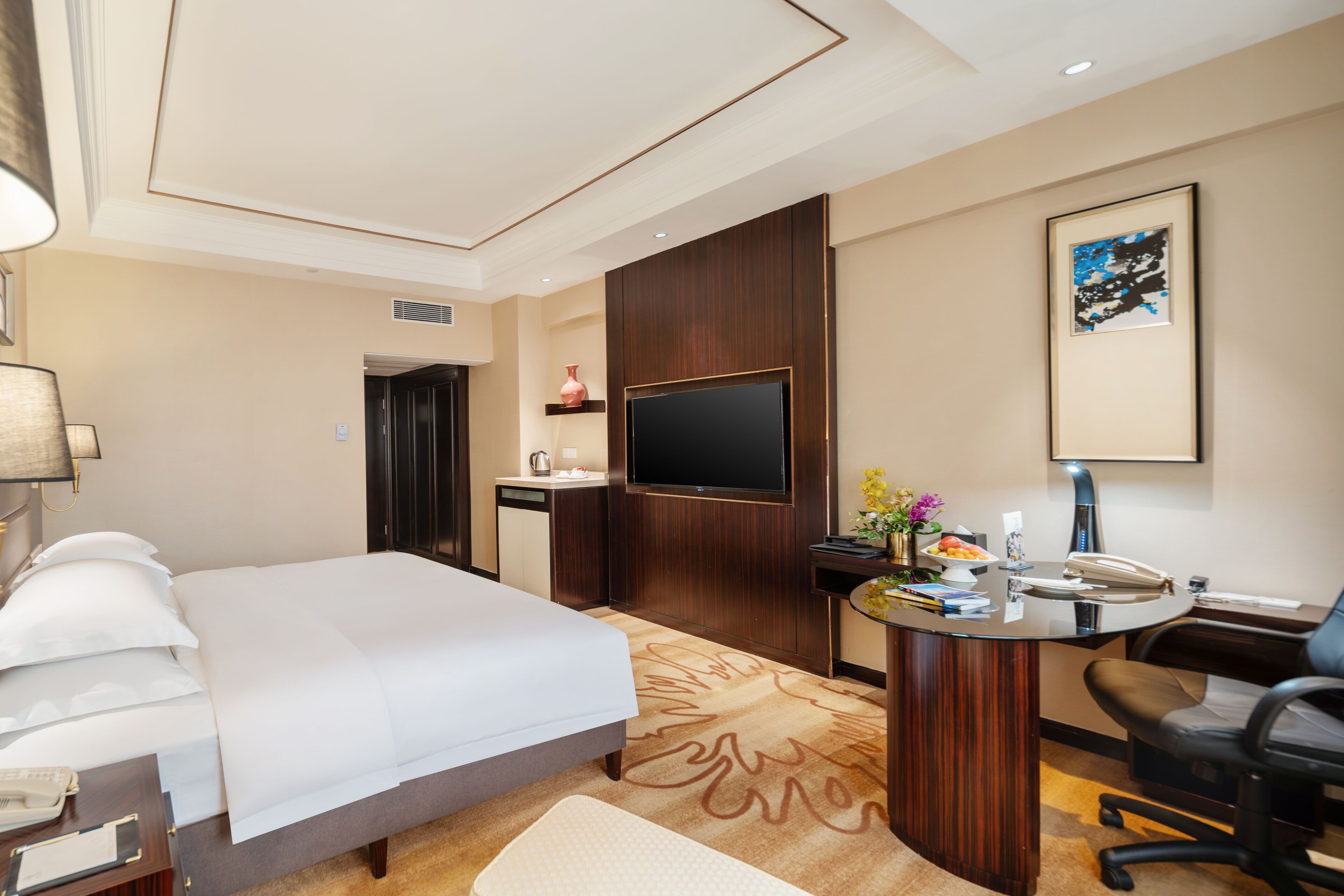 Habitación de hotel con cama, escritorio, silla, televisor y una pequeña kitchenette.